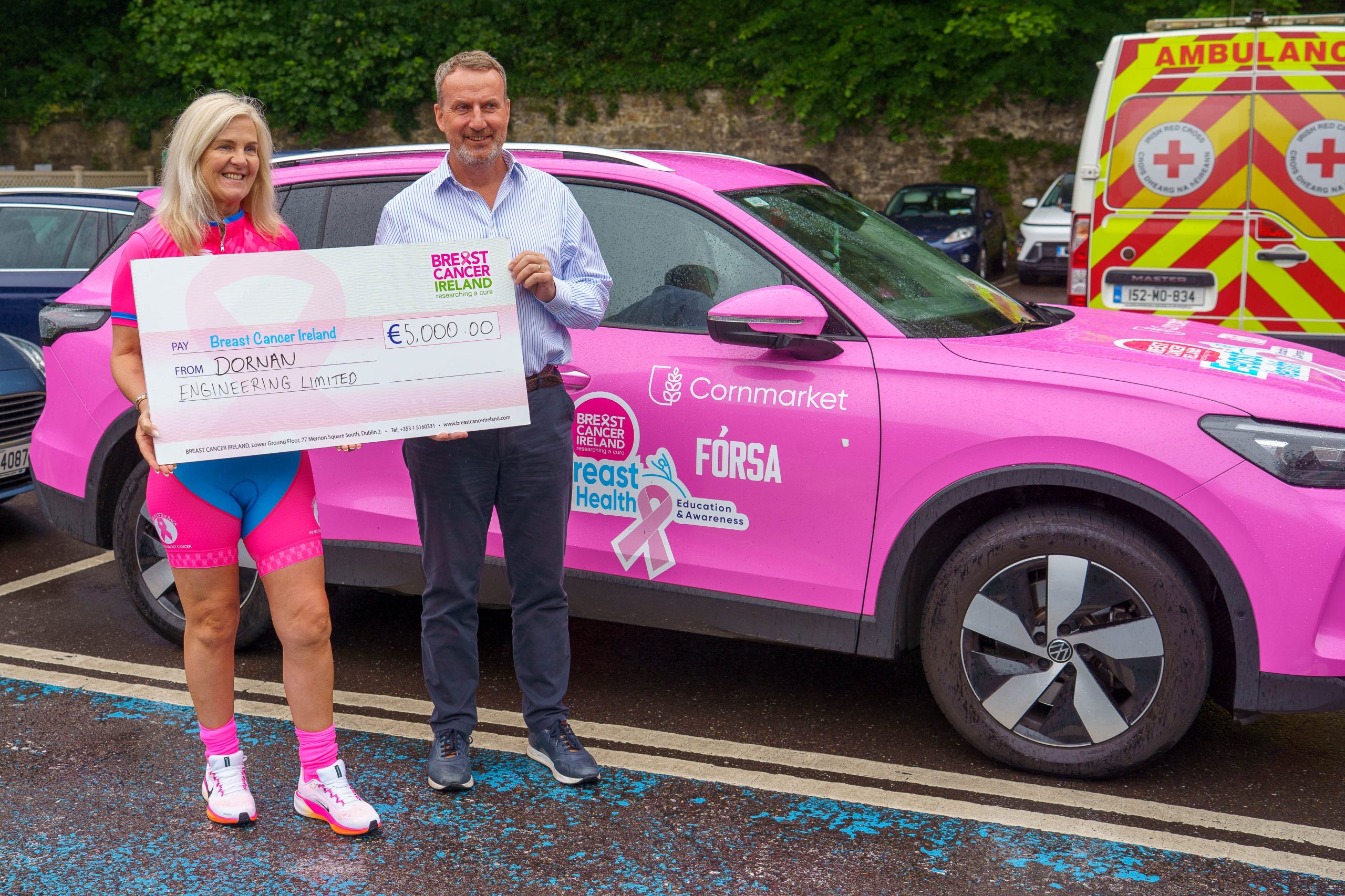 Micheál O Connor standing in for a photo with Breast Cancer Ireland rep handing over a cheque to support the work they do